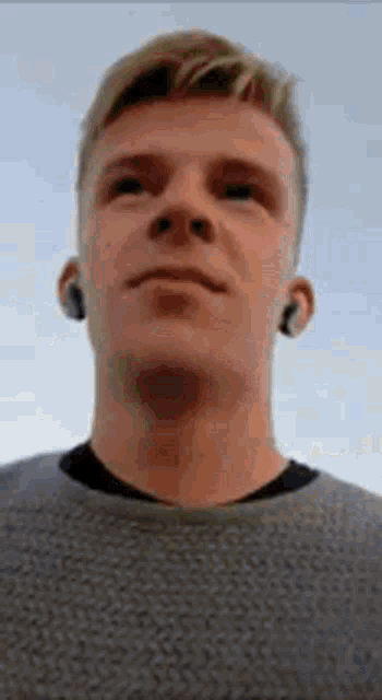 a young man wearing ear buds and a sweater is looking up at the camera .
