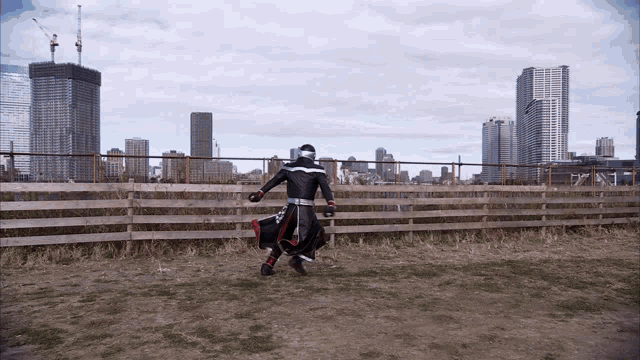 a man in a superhero costume stands in front of a wooden fence with a city in the background