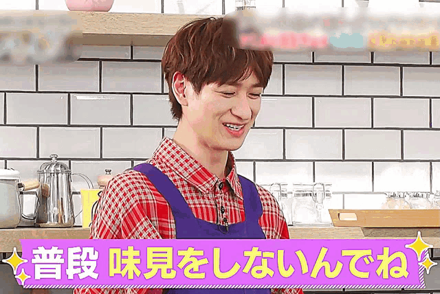 a man wearing a plaid shirt and an apron is smiling in a kitchen with chinese writing