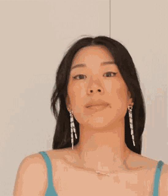 a woman wearing a blue tank top and earrings is making a funny face .