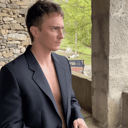 a man in a suit without a shirt is looking out a window