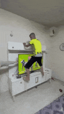a man in a yellow shirt is standing on a television stand