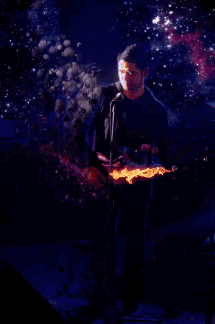 a man is singing into a microphone while holding a guitar that is on fire