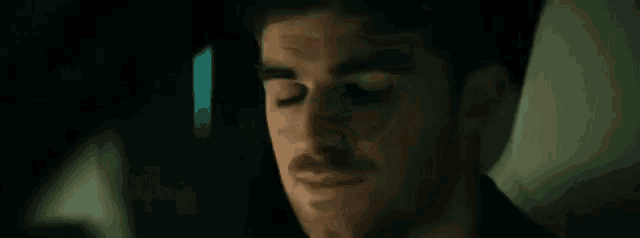 a close up of a man 's face with a beard looking at the camera in a dark room .