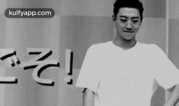 a man in a white t-shirt is standing with his hands on his hips in a black and white photo .