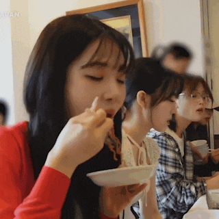 a woman in a red shirt is eating noodles from a white bowl