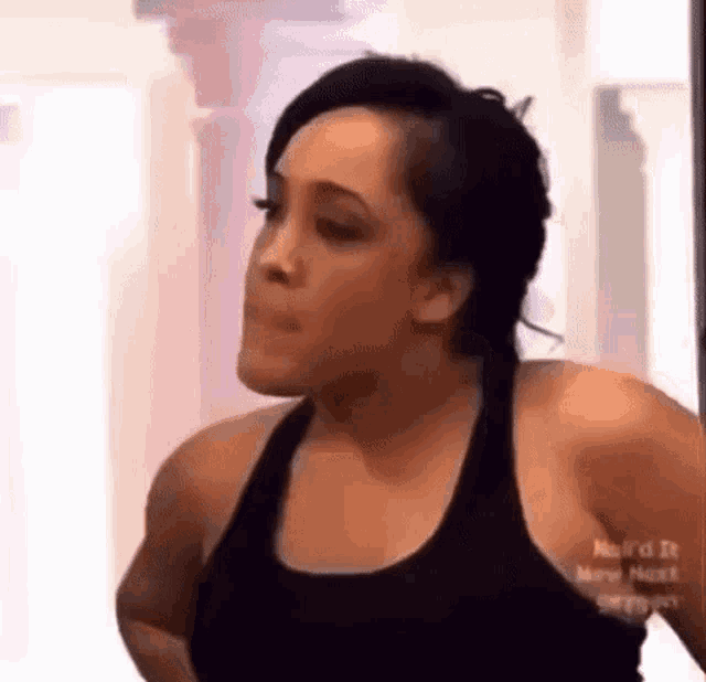 a woman in a black tank top is making a funny face while standing in a room .