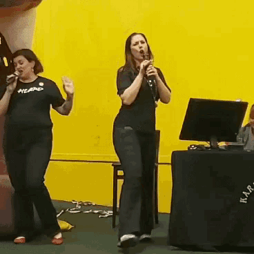 a woman singing into a microphone wearing a black shirt that says heard