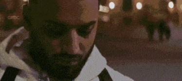 a man in a white hoodie is talking on a cell phone in a city at night