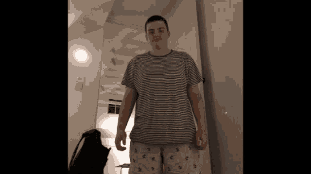 a man wearing a striped shirt and shorts stands in front of a mirror