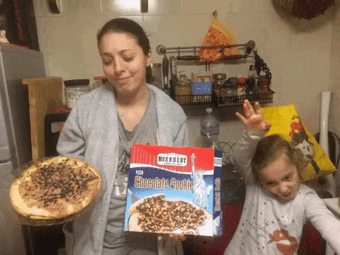 a woman holding a box of chocolate cookie pizza next to a child