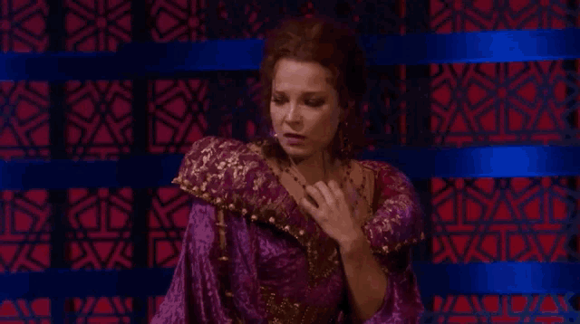 a woman in a purple dress and gold jewelry is standing in front of a red and blue wall .