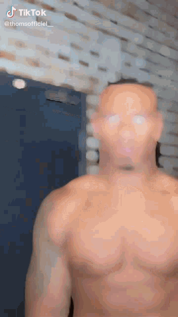a man without a shirt is standing in front of a brick wall and a door .