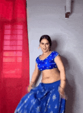 a woman in a blue crop top and blue skirt is dancing in front of a window .