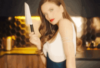 a woman is holding a large knife in her hand and looking at the camera .