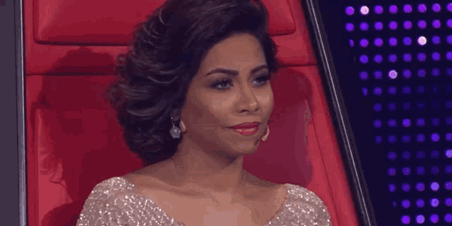 a woman in a sequined dress is sitting in a red chair and smiling .
