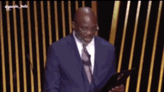 a man in a suit and tie is standing in front of a microphone reading a book .