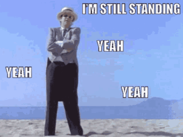 a man in a suit and hat is standing on the beach and says yeah