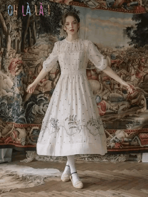 a woman in a white dress stands in front of a tapestry with the words oh la la on it