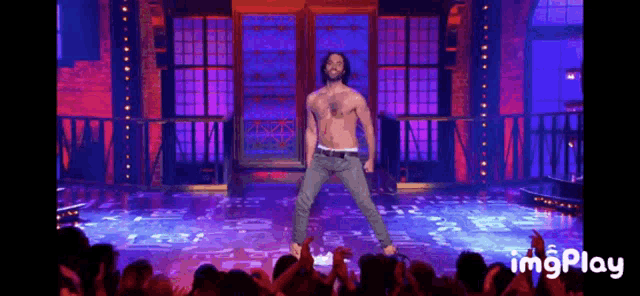 a man without a shirt is dancing on a stage in front of a crowd of people .