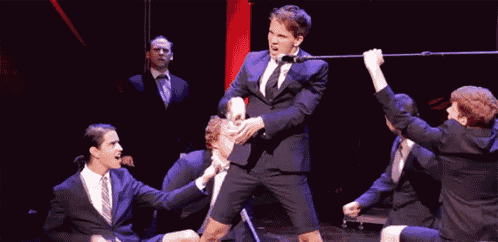 a man in a suit and tie is dancing on a stage with other men .