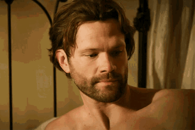 a shirtless man with a beard looks down