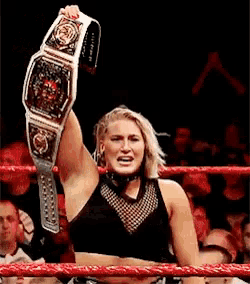 a woman in a wrestling ring is holding a championship belt