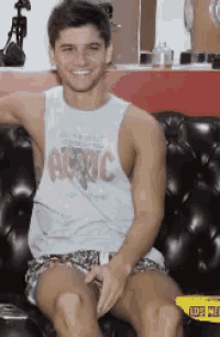 a man wearing a tank top that says ac/dc is sitting on a black couch