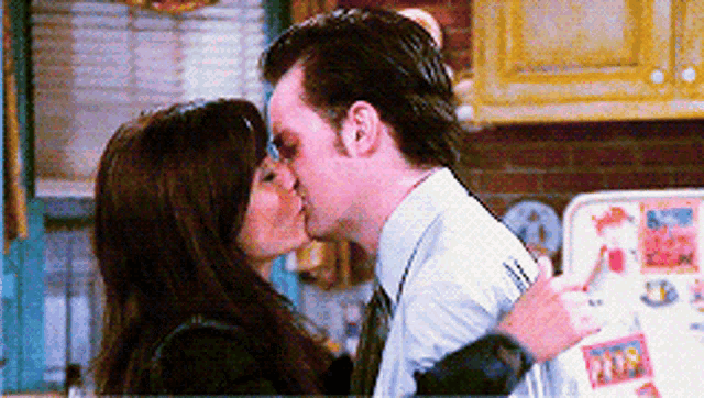 a man and a woman are kissing in front of a refrigerator with a sticker on it that says ' ice cream '