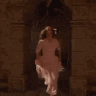 a woman in a pink dress is standing in a room with her hands on her hips .