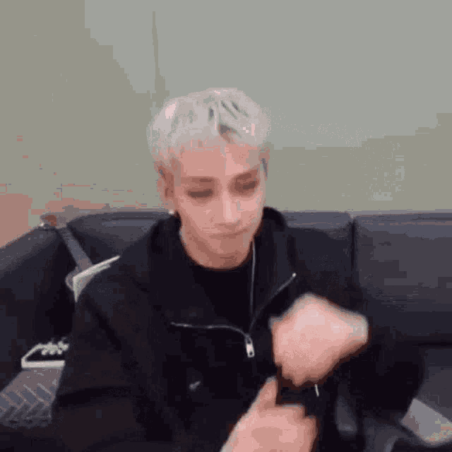 a young man is sitting on a couch wearing a black jacket and headphones .
