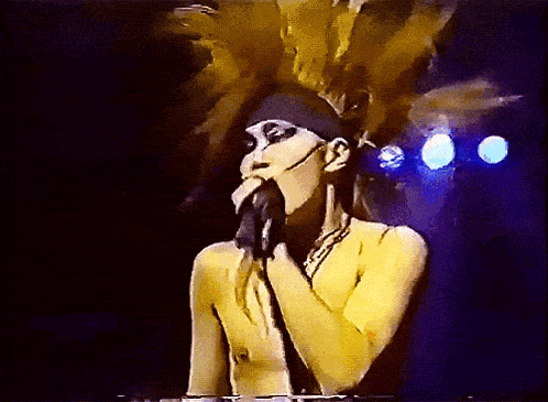 a naked woman singing into a microphone with feathers in her hair