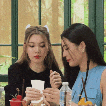 two women are sitting at a table with a bottle of water in front of them