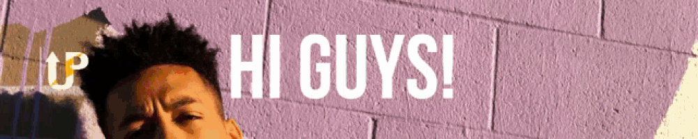 a man is standing in front of a purple brick wall with the words hi guys written on it