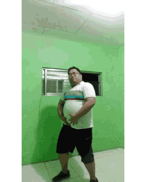 a man standing in front of a green wall with his hands on his belly