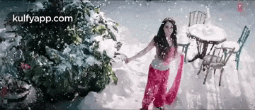a woman in a red dress is standing in the snow in front of a christmas tree .