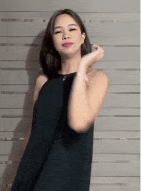 a woman in a black dress stands in front of a gray wall
