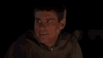 a man is making a funny face in the dark while sitting at a table .