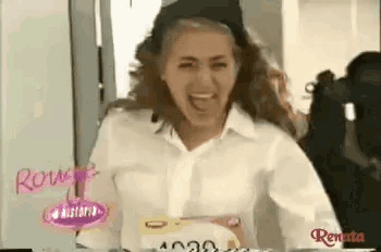 a woman wearing a white shirt and a black hat is laughing and holding a cake .