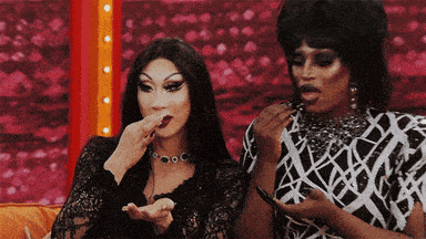 two drag queens are sitting next to each other and one of them is eating something