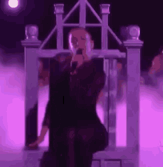 a woman in a black dress is singing into a microphone while sitting on a purple throne .