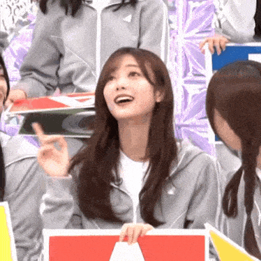 a girl in a gray jacket is smiling and pointing upwards