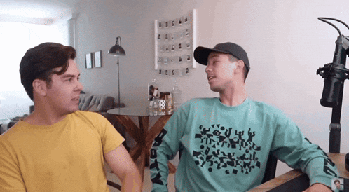 two men are sitting in front of a microphone and one of them is wearing a shirt that says ' a '