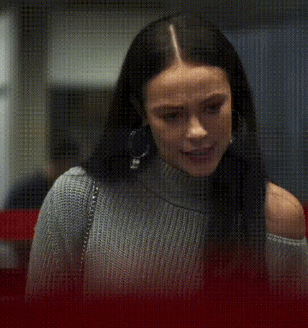 a woman wearing a gray sweater and hoop earrings is screaming .