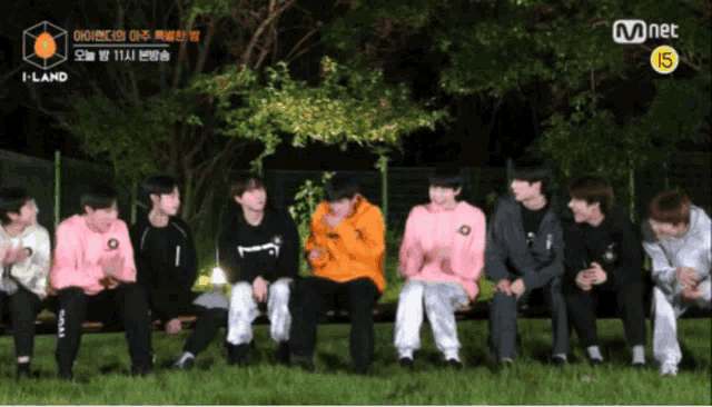 a group of young men are sitting on a bench in the grass with a mnet logo in the background