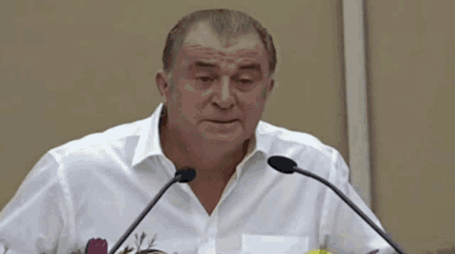 a man in a white shirt is giving a speech in front of two microphones .