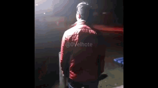 a man in a red jacket is standing in front of a red car at night .