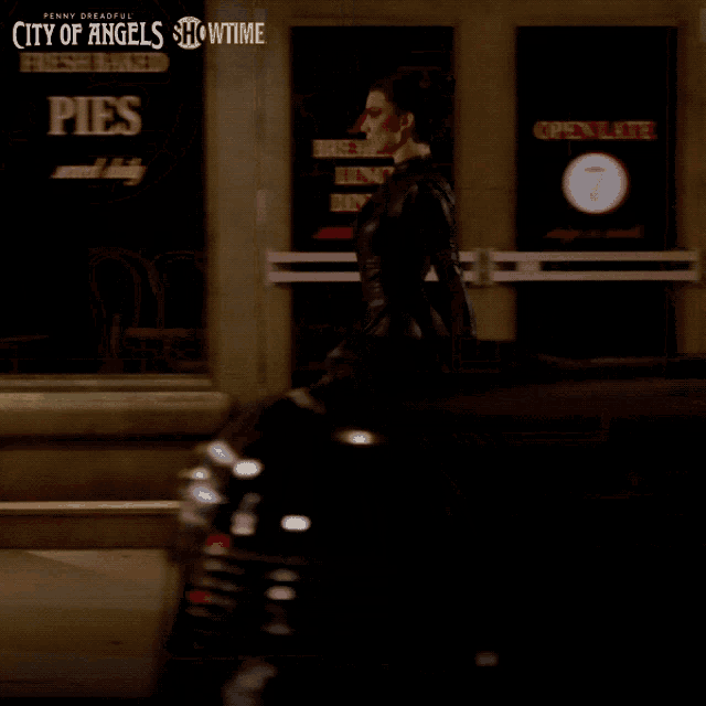 a woman in a long black dress walks past a coffee shop