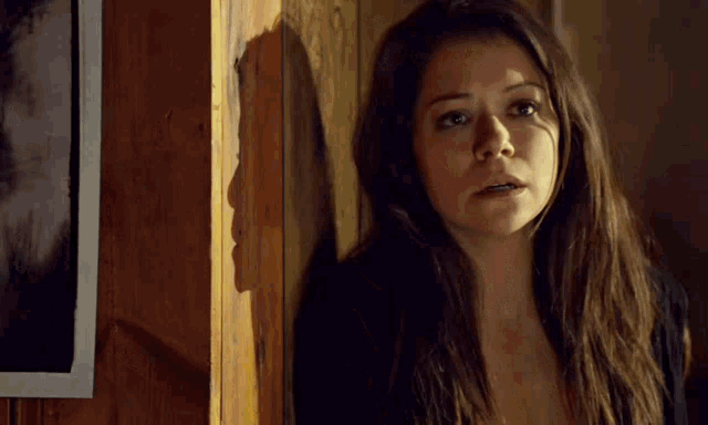 a woman is standing in front of a wooden wall looking at the camera .