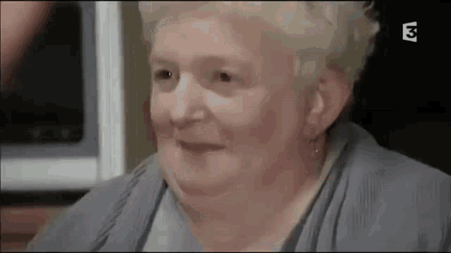 a close up of an elderly woman making a funny face while sitting in front of a microwave .